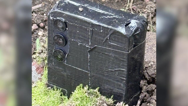 What appears to be an Android phone covered in black tape buried in a yard 