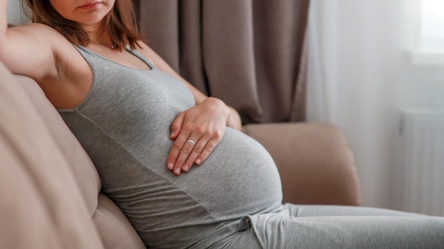 Pregnant woman visibly uncomfortable and in pain, seated on cozy living room sofa at home 