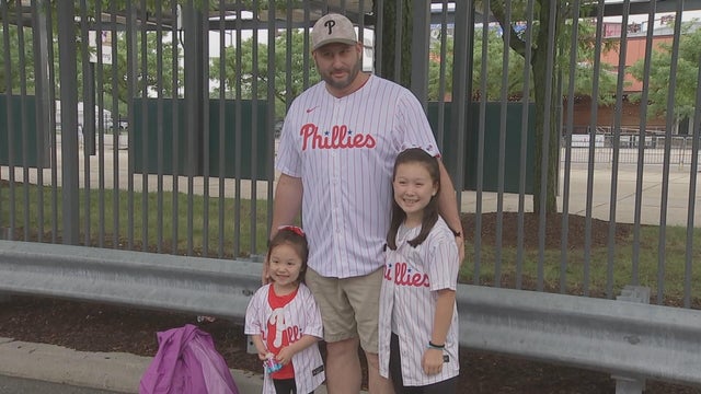 A man and two little girls post for a photo near Citizens Bank Park, they're all wearing Phillies jerseys 