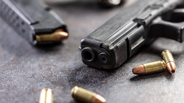 Close-up of a black metal 9mm automatic pistol with bullets all placed on a concrete table 