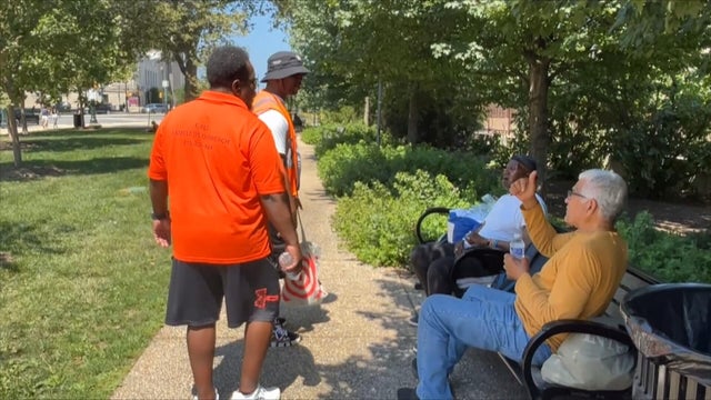 A person on a bench gives a thumbs up to two homeless outreach workers in a park near Center City Philadelphia 