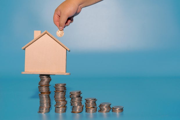 Hand inserting coin into house model on top of coins stacks. Save and investment money concept. 