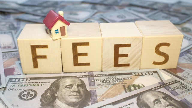 "FEES" text on wooden cubes with money dollars background and tiny model of house 