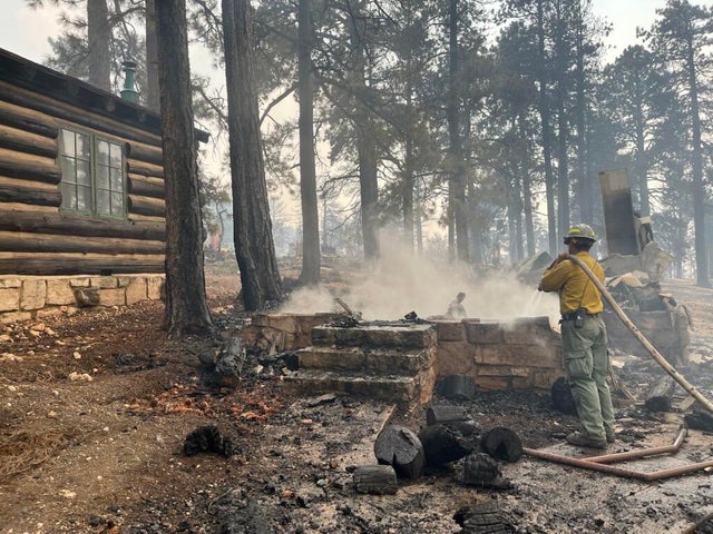 A firefighter stands near smoldering debris and active flames amid the charred remains of a burned structure near the Grand Canyon Lodge. Grand Canyon National Park posted the photo on Facebook on July 13, 2025. 