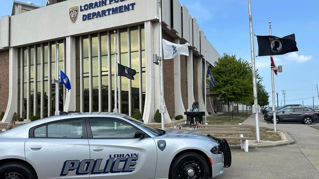 Candles sit on a memorial and flags fly at half-staff outside the police department in Lorain, Ohio, on July 24, 2025, a day after a deadly ambush. 