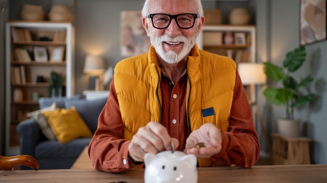 Senior man saving money using piggy bank at home 
