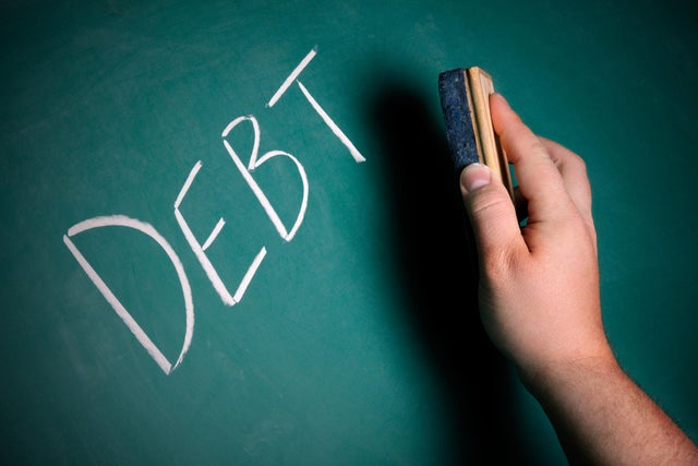 Hand preparing to erase the word DEBT from a chalkboard 