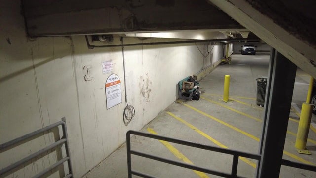 An individual sleeps on a bench inside a Toms River municipal parking lot 