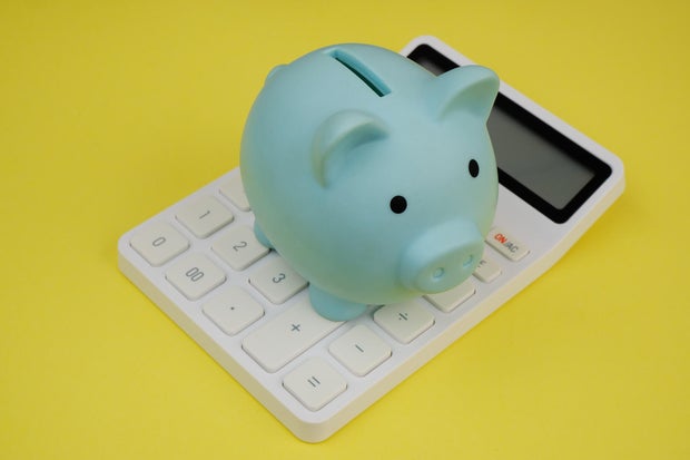 Blue piggy bank on white calculator on yellow background. 