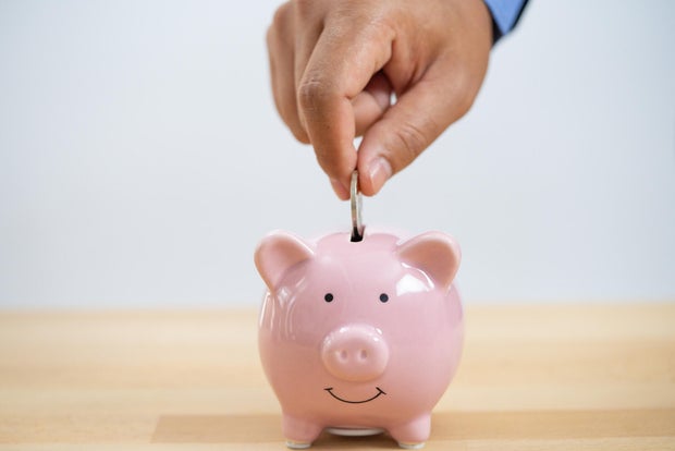 Businessperson's Hand Putting Coin In Piggybank