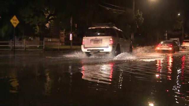 Cars drive down a flooded street 