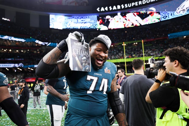 Fred Johnson (74) of the Philadelphia Eagles celebrates after Super Bowl LIX against the Kansas City Chiefs, he's wearing the Super Bowl baseball hat and holding up the front page of the Times-Picayune, which says champs in all caps 