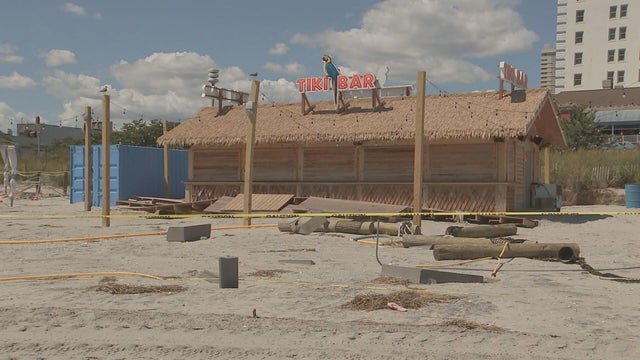 Caution tape is around a shuttered beachfront bar, debris is seen on the sand outside the bar 