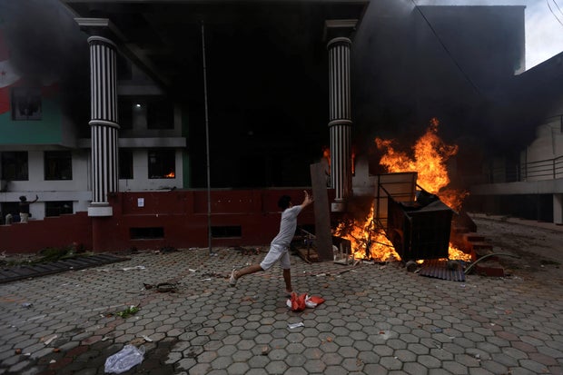 A demonstrator throws a wooden plank towards flames outside Nepali Congress party office, in Kathmandu 