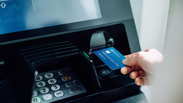 Close up of young woman inserting her bank card into automatic cash machine in the city. Withdrawing money, paying bills, checking account balances, transferring money. Privacy protection, internet and mobile security concept 
