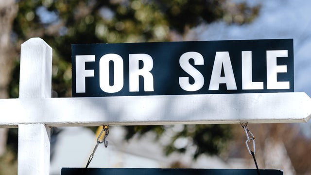 For Sale Sign Hangs in Front Yard of House 