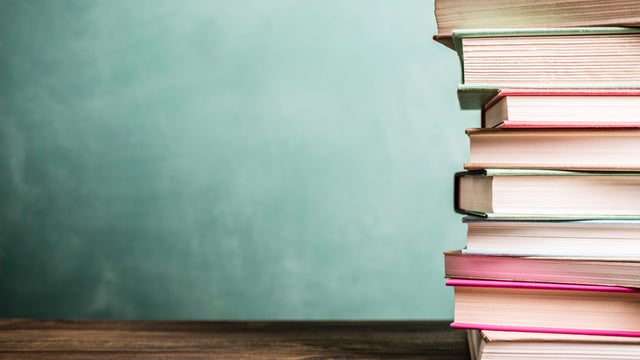 Textbooks stacked on school desk with chalkboard background. 