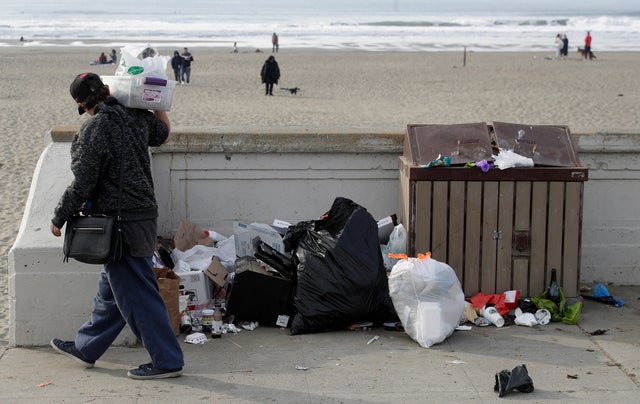 A woman walks past trash piled next to a garbage bin at Ocean Beach in San Francisco on Jan. 3, 2019. 