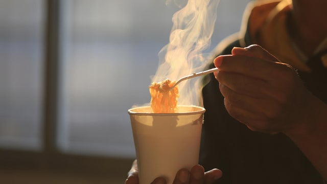 Man hand holding plastic fork of instant noodles with smoke rising in the home sunset background, Sodium diet high risk kidney failure, Healthy eating concept 