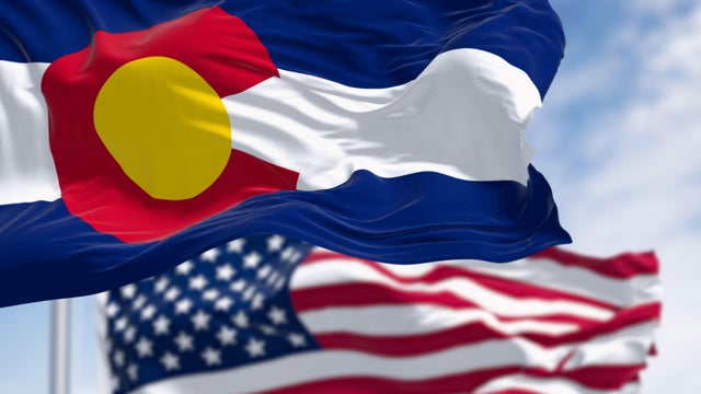 Colorado and US flags waving in the wind on a clear day 