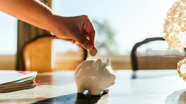 Woman putting savings in a white piggy bank. 