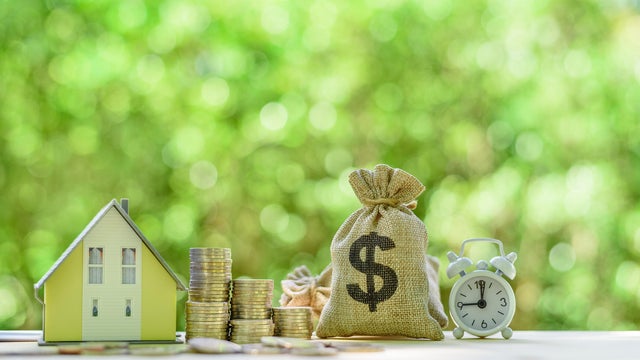 Mortgage-backed security MBS, financial concept : House model, stacks of rising coins, US dollar, money bags, a clock on a table over green background, depicts investment in home bought from the bank 