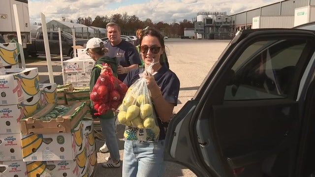 Someone carries two bags of fruit to a car at the Food Bank of Delaware 