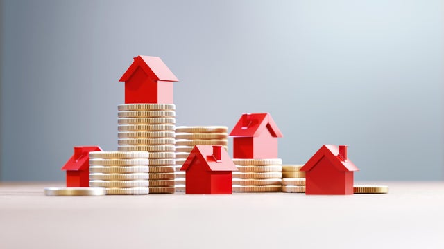 Red House Objects Over Coin Stacks Before Defocused Background - Real Estate And House Rental Concept 