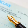 Close up of an ink pen and a cheque book. 