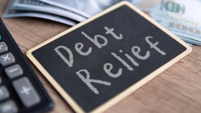 A blackboard with Debt Relief written in chalk, a calculator and US dollar bills. 