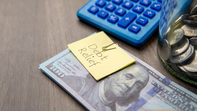 A stack of US hundred-dollar bills with a DEBT RELIEF note. 