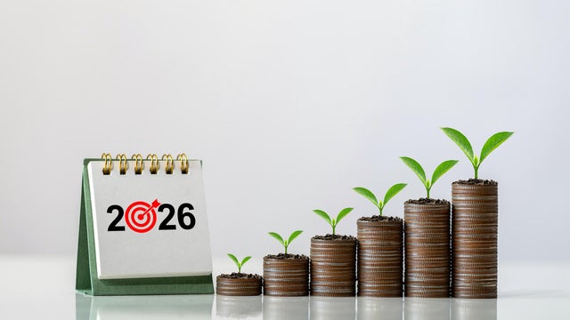 2026 desk calendar next to ascending stacks of coins with green seedlings on a white background, symbolizing financial planning, investment strategy, economic growth, and New Year wealth building. 