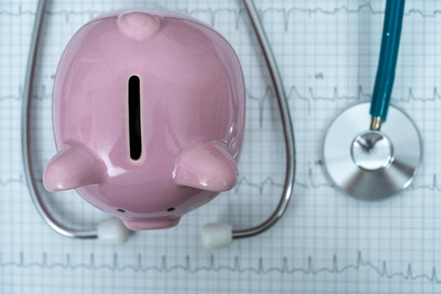Piggy bank with stethoscope on illustration of wave form on checked ecg graph background, health saving account, insurance, top view 