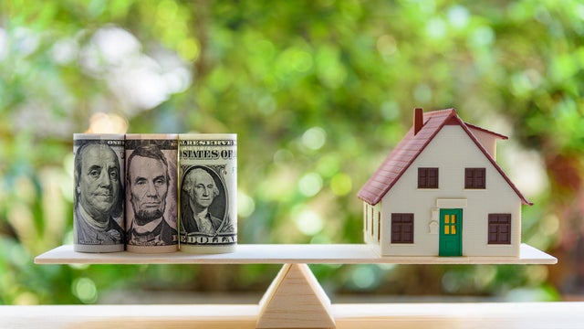 Home loan / reverse mortgage or transforming assets into cash concept : House model, US dollar notes on a simple balance scale, depicts a homeowner or a borrower turns properties / residence into cash 