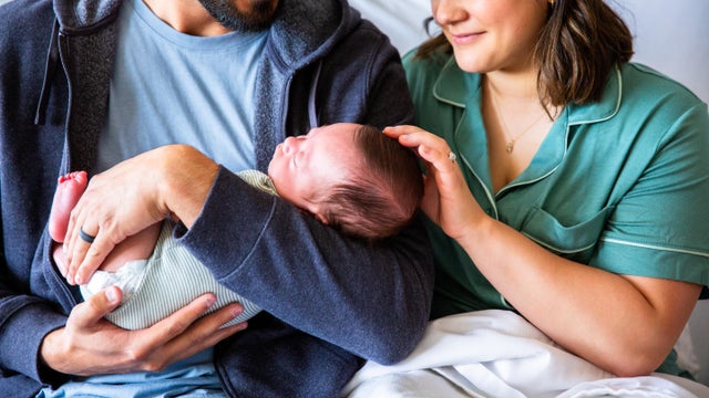Young parents holding their newborn baby boy in the hospital bed 