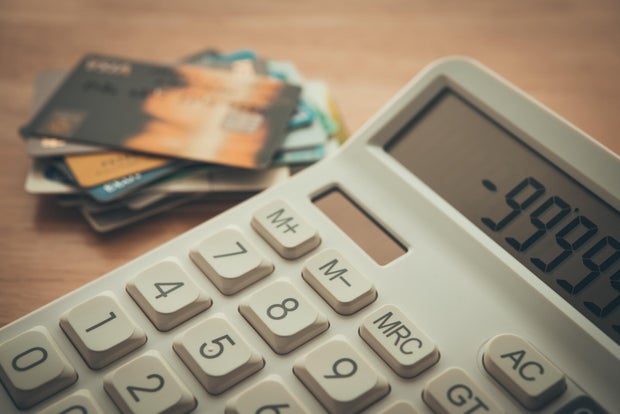 White calculator shows minus delinquent and many credit cards on wooden table background. 
