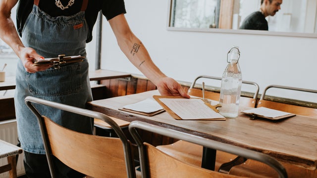 A male employee places menus onto tables in a cafe 