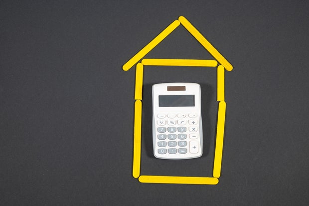 Concept of buying a house: a c calculator inside a drawing of a house made of yellow sticks.