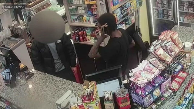 Elijah Brown holding a phone to his ear behind a bodega counter 