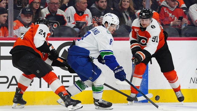 Vancouver Canucks' Conor Garland, center plays the puck past Philadelphia Flyers' Nick Seeler (24) and Carl Grundstrom (91) during the first period of an NHL hockey game 