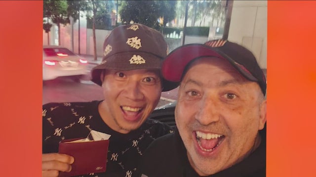 Two men with hats smiling as one holds up a wallet 