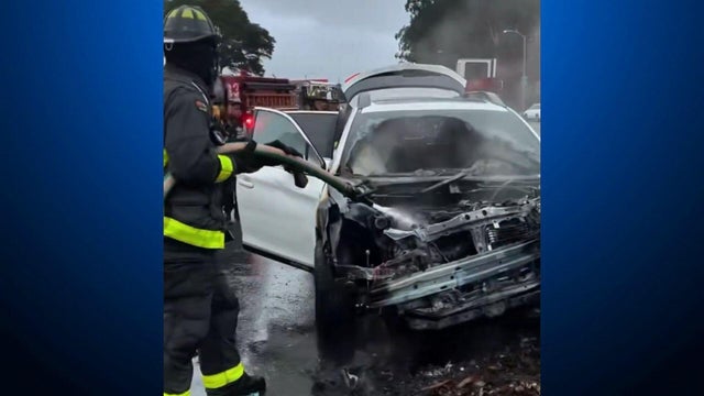A firefighter holding a hose that is spraying water on a damaged vehicle 