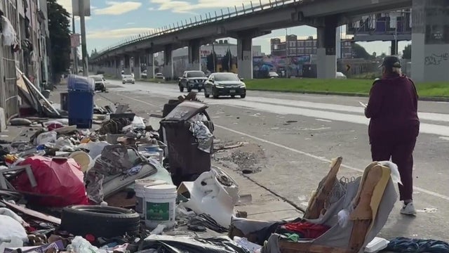 A woman walks by a pile of trash left on the side of a roadway 