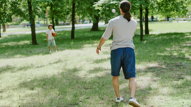 Father Playing Catch with Young Child Outdoors in Green Park 