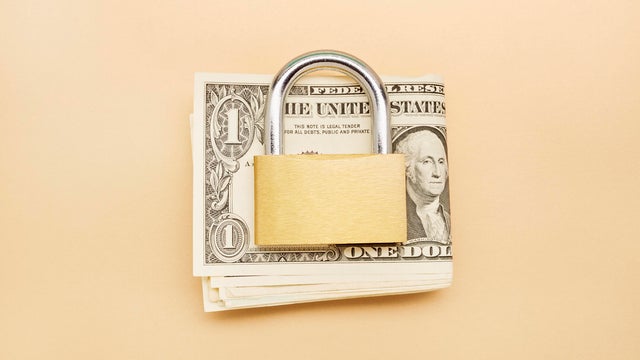 High angle view of a bunch of American Dollar banknotes and closed padlock on beige background 