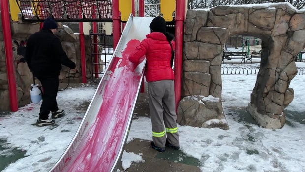 A city worker washes red paint off a slide on a playground