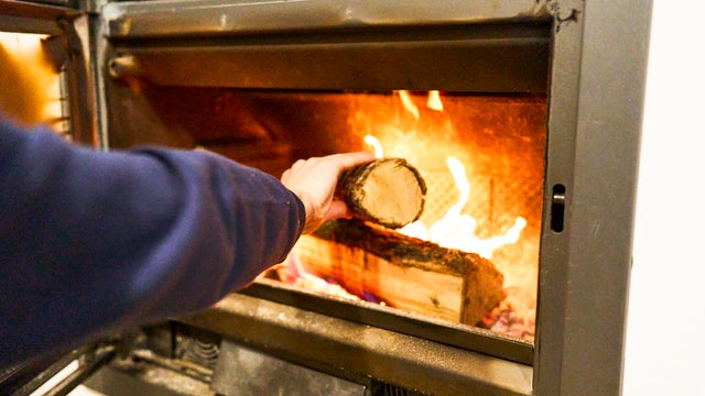 Person fueling wood stove with burning log 