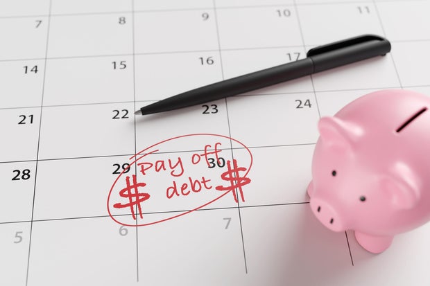 A pink piggy bank, a pen and a calendar marked with the word pay off debt and dollar signs in red on a date. Illustration of the concept of financial debt, loans and owing money 