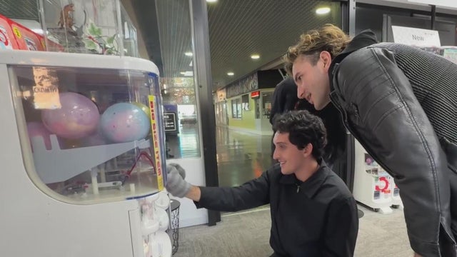 Two people in front of a gacha coin machine 