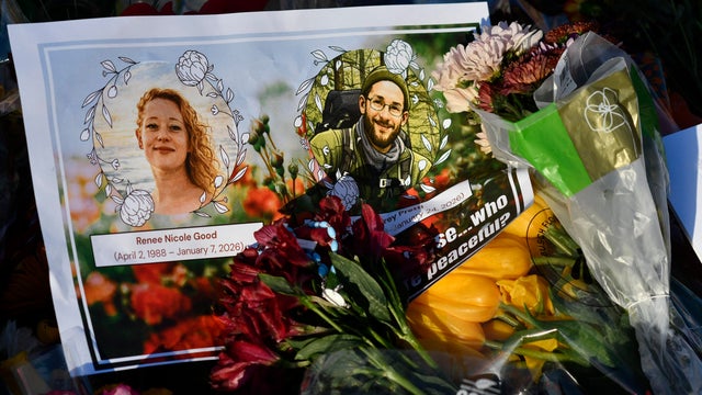 A card with photos of Renee Good and Alex Pretti and flowers at a memorial in Minneapolis, 